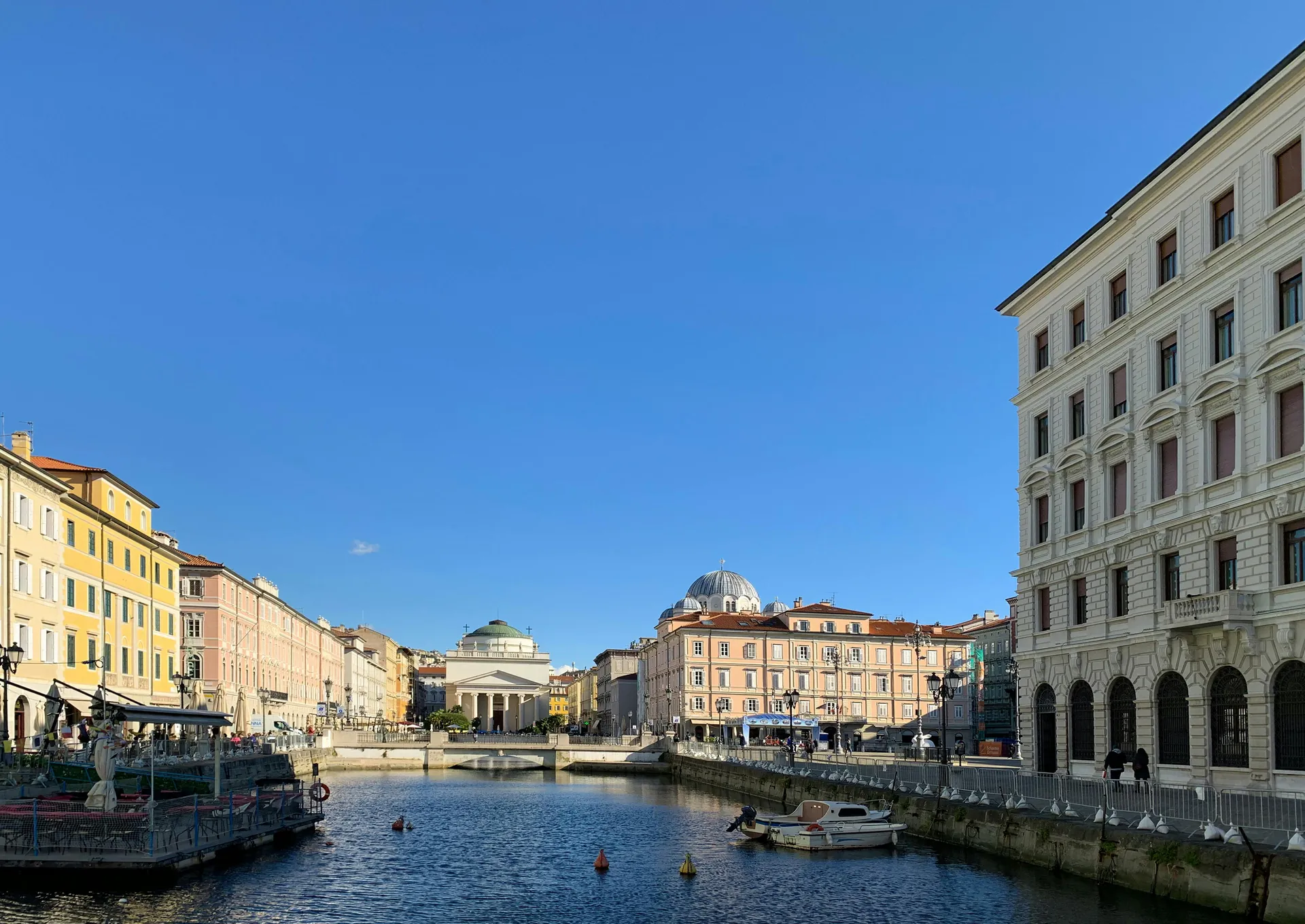 Beautiful view of the canal and historic buildings in Trieste, Italy under a clear blue sky.