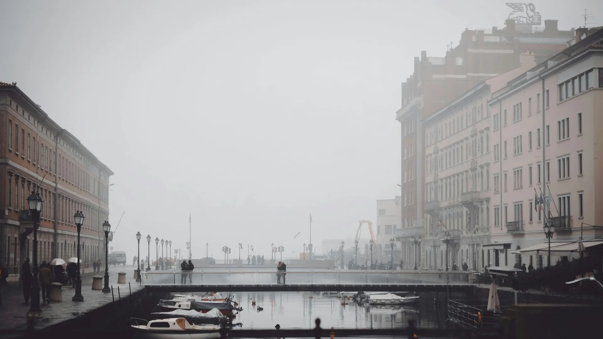 Misty day over a canal in Trieste, Italy, showcasing historic architecture and boats.