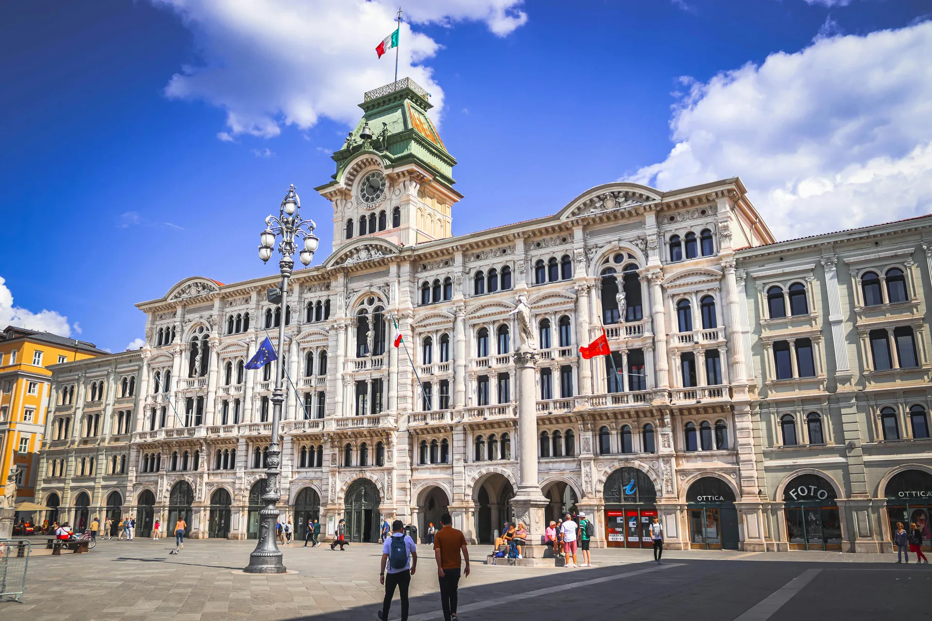 Daytime shot of Trieste City Hall's elegant architecture in Italy with people and flags displayed.